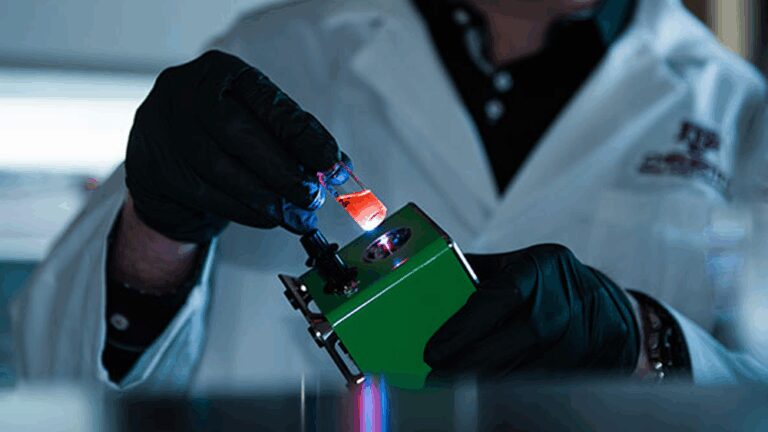 A scientist in a lab coat and dark gloves using equipment.
