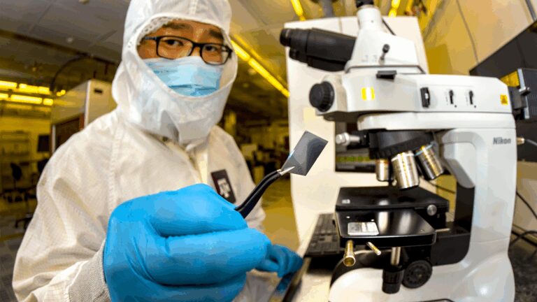 A man in scrubs and a mask using a microscope
