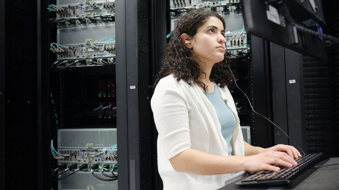 A girl in a server room typing at a computer.