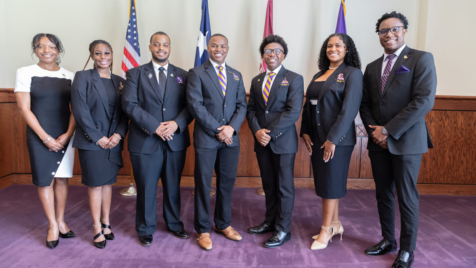 A group of well-dressed Prairie View A&M University students standing in front of flags.