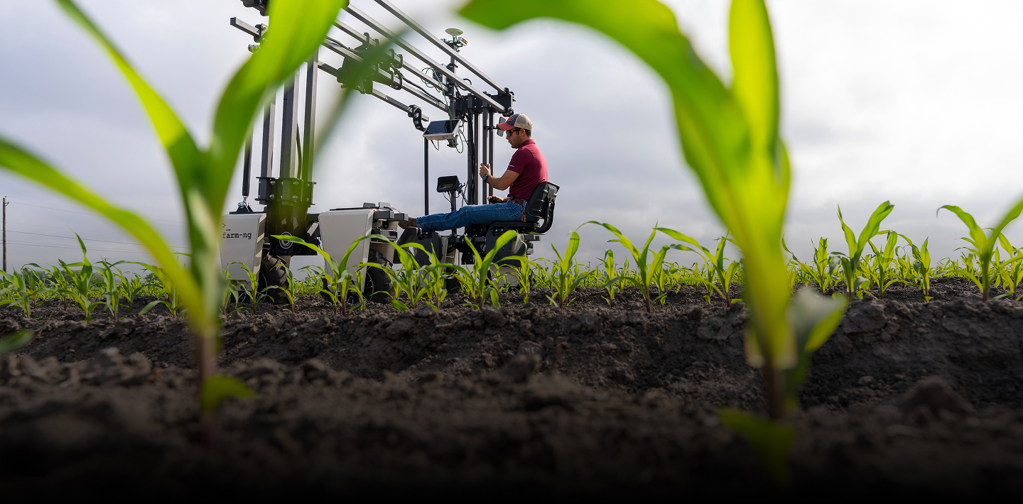 Man in a field operates a machine, with green sprouts framed in the foreground