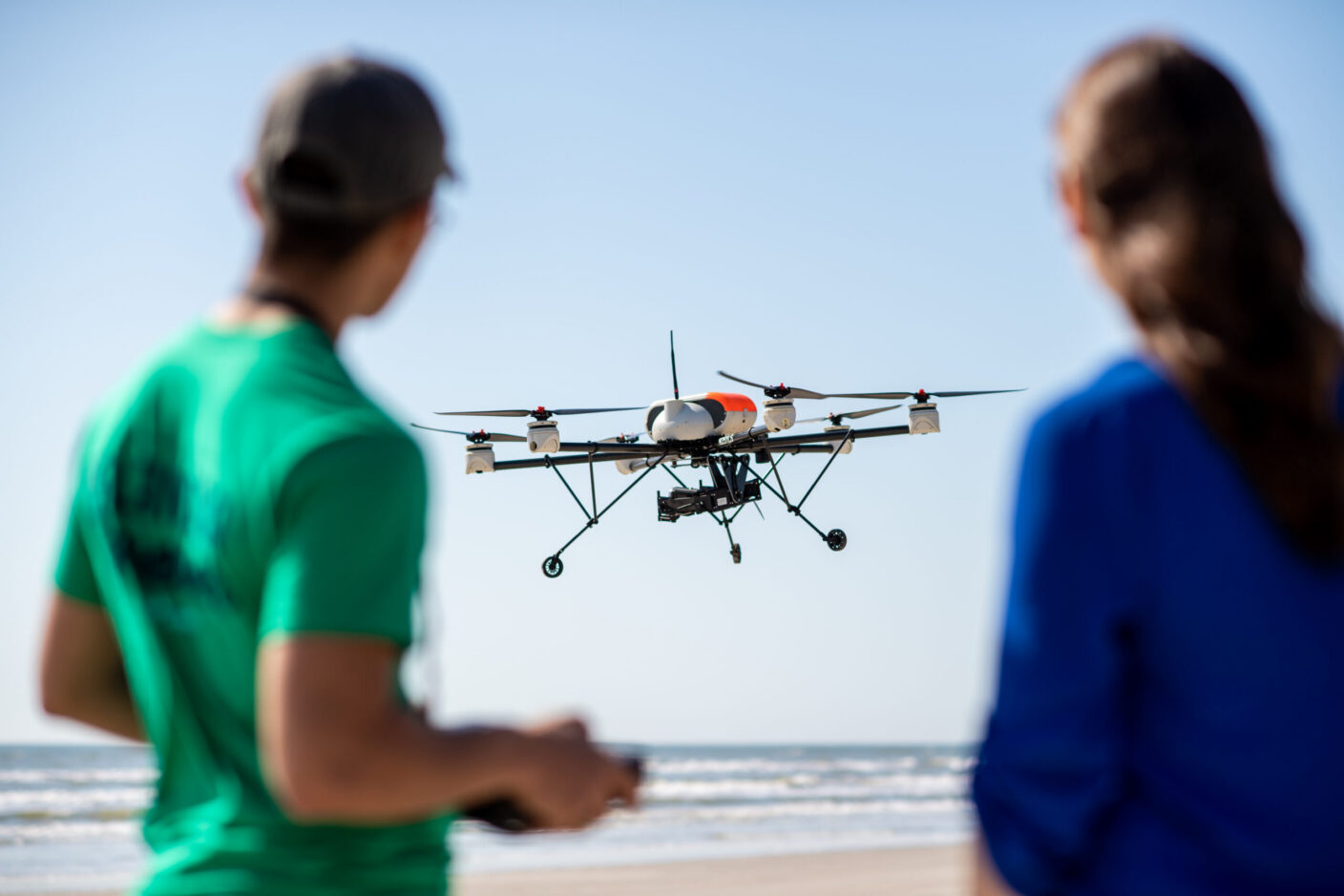 Two individuals operating a drone with the ocean in the background.