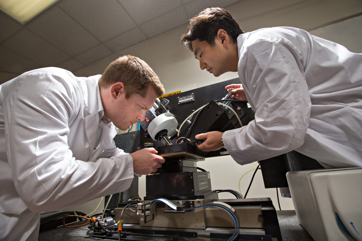 Two people in white lab coats working on a device