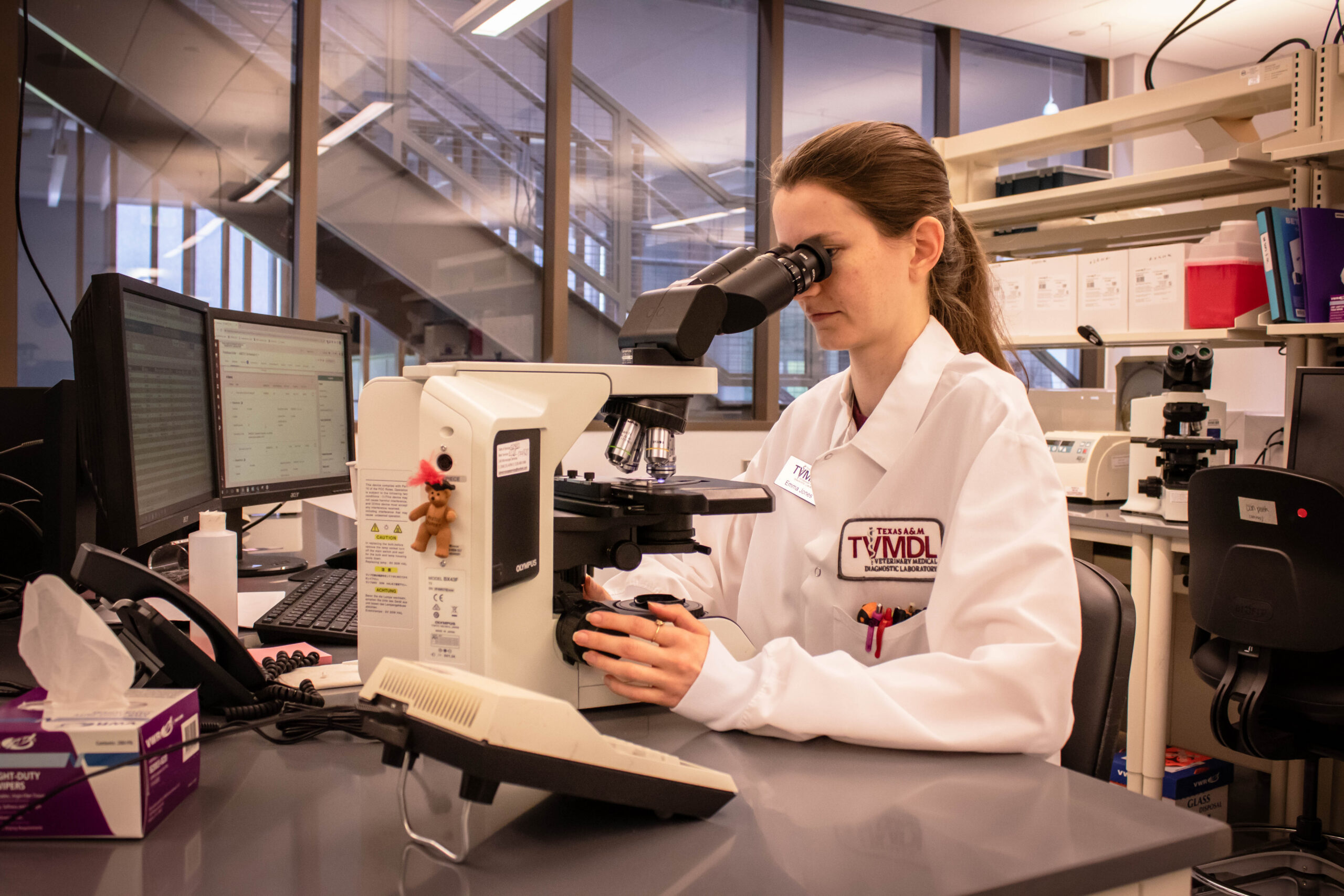 A scientist in a lab coat examines a specimen through a microscope in a modern laboratory setting.