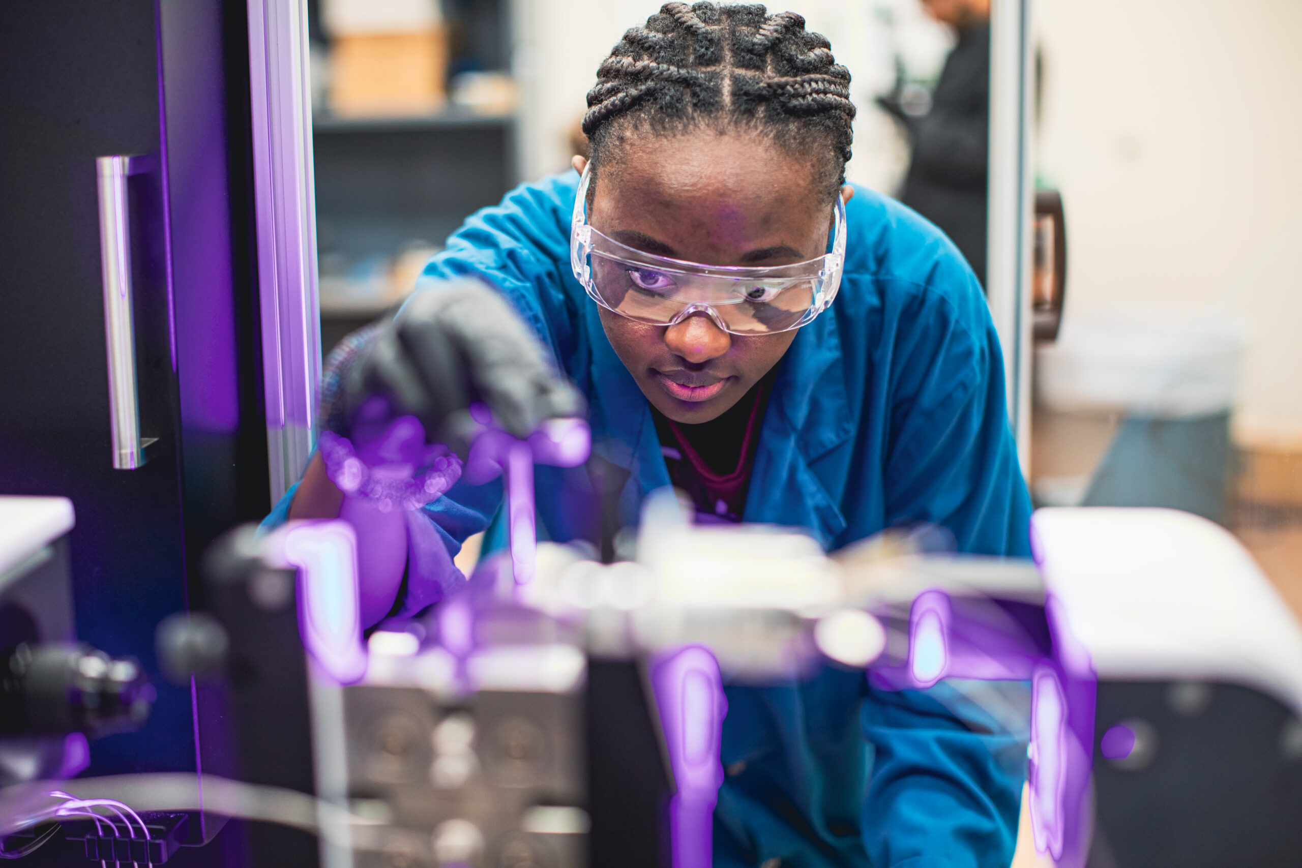 A student in protective clothing and safety goggles working on a machine.