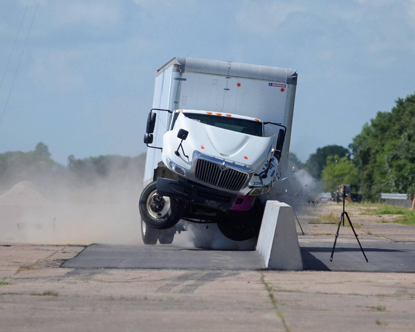 A white semi-truck crashes into a concrete barrier, sending debris flying and kicking up dust.