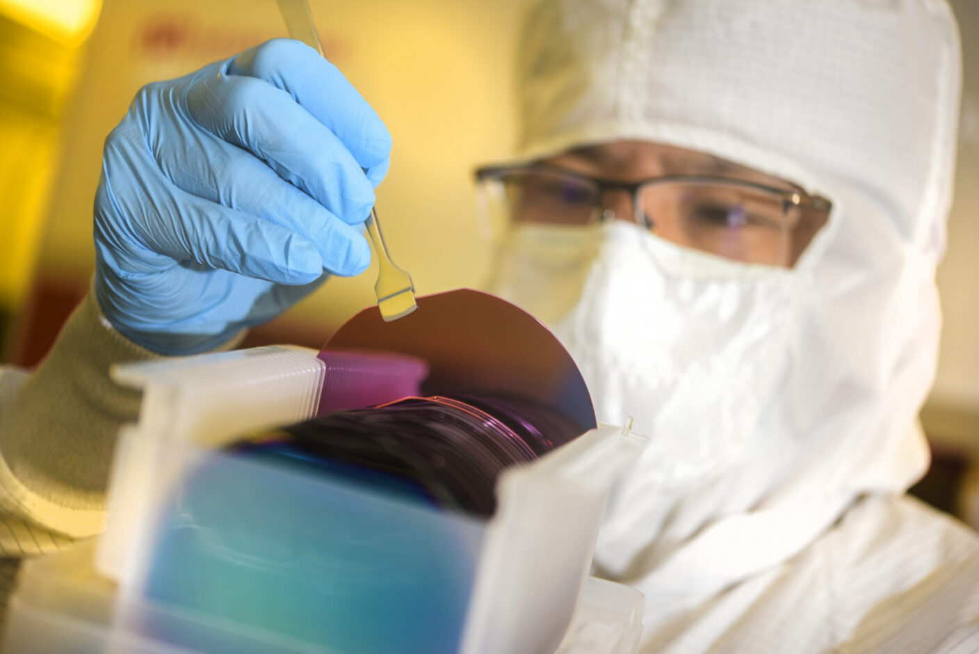 A technician in a cleanroom suit handles a semiconductor wafer with precision tools.