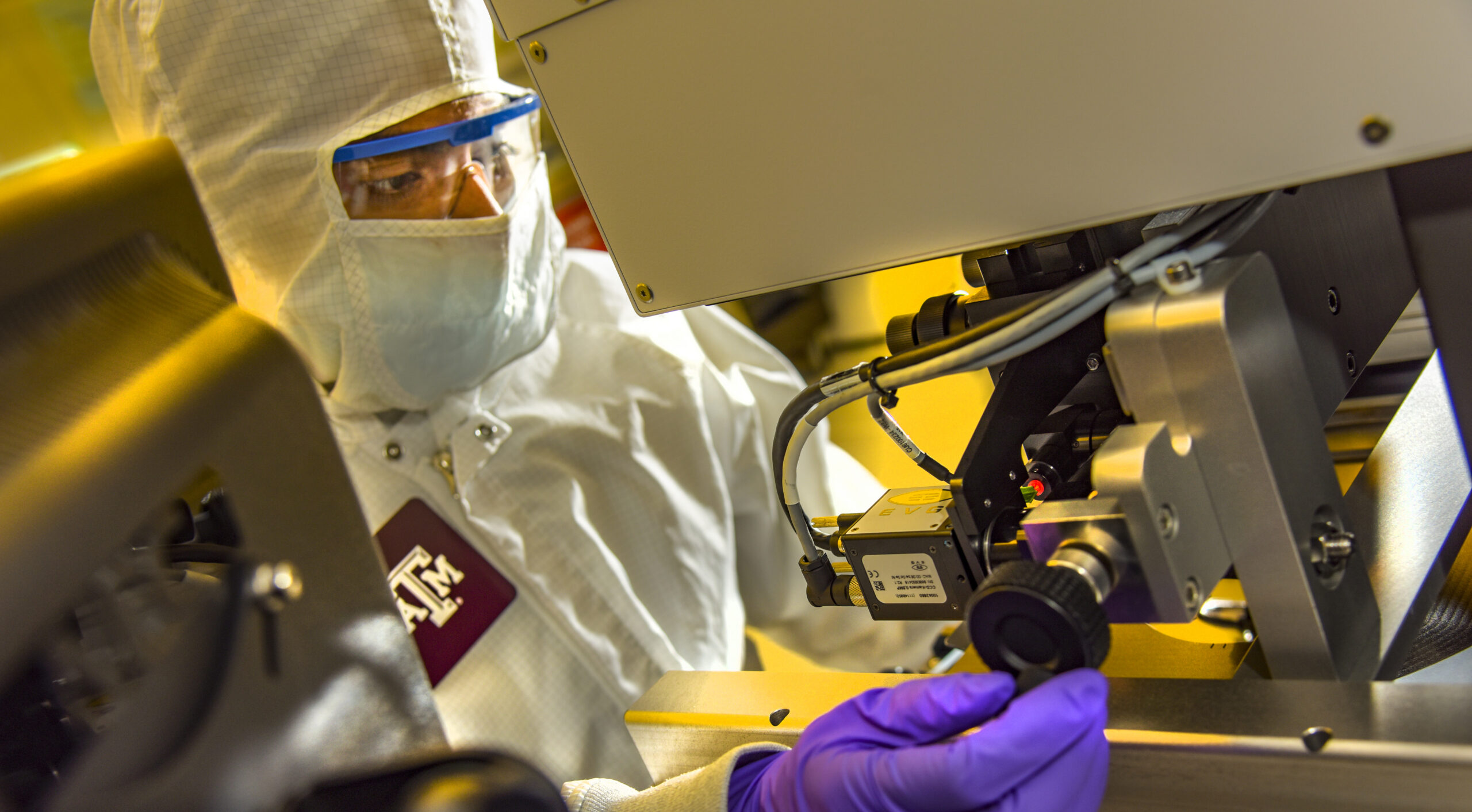A technician in a cleanroom suit and gloves operates equipment with precision.