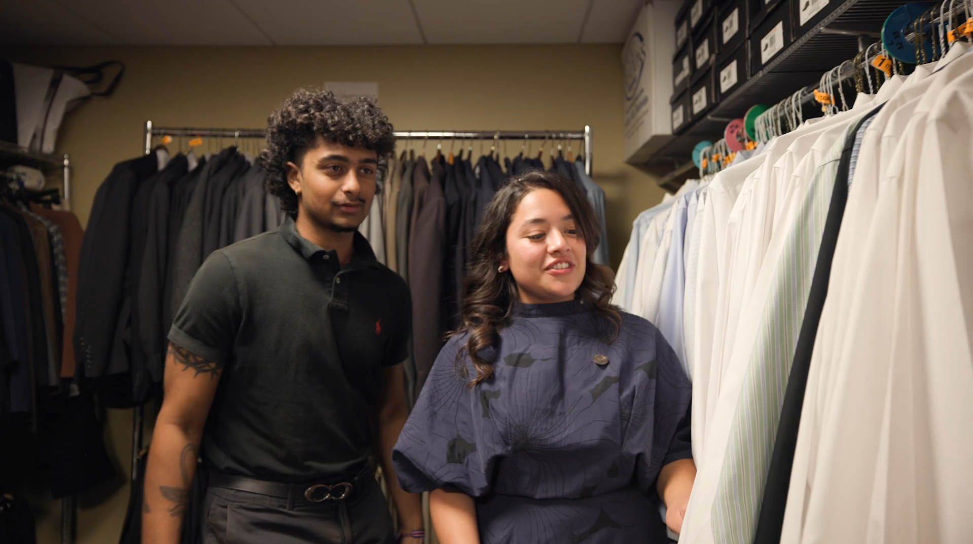 Two people looking through a rack of white collared shirts on hangers (a career closet)