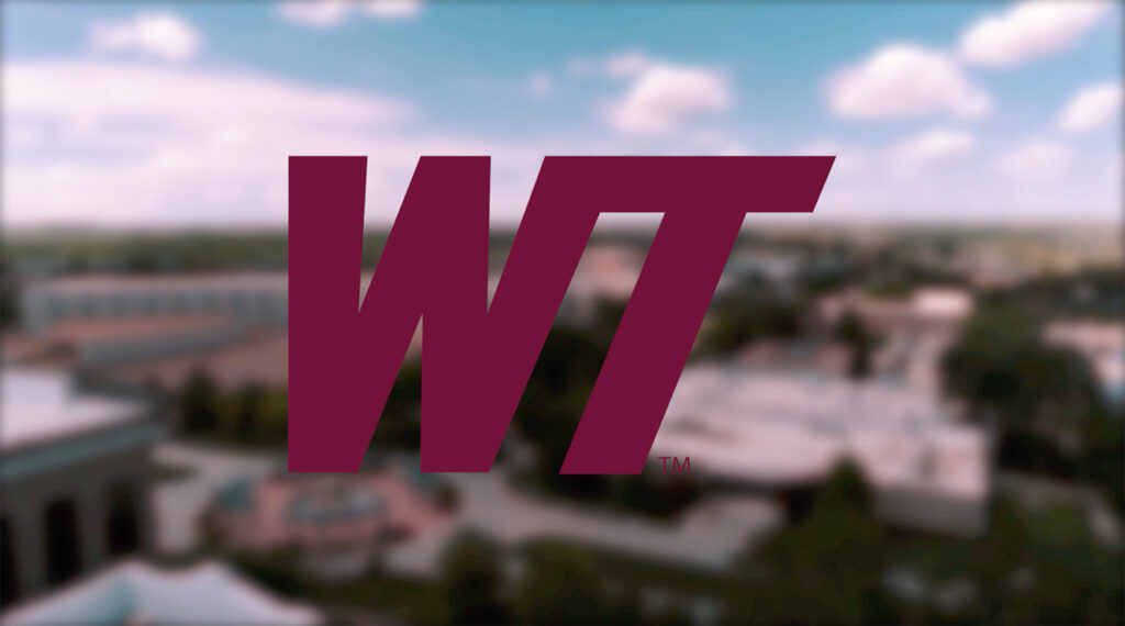 West Texas A&M University’s maroon “WT” logo displayed over a blurred aerial view of the university campus under a blue sky with scattered clouds.